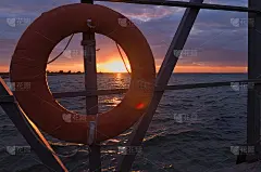老码头上的救生圈，背景是彩色的日落和波浪起伏的大海。夕阳西下时，绑在码头铁栏杆上的救生圈。明信片设计
