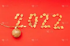 由五颜六色的糖果和红色背景上的金色圣诞球组成的数字2022
