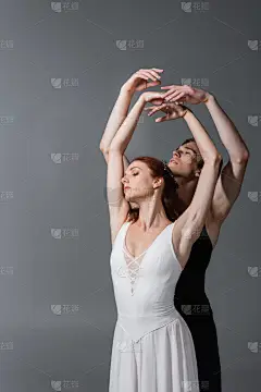 优雅的芭蕾舞演员，身穿白衣，与舞伴共舞，同时在深灰色的衣服上举手表决