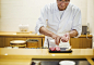 A chef working in a small commercial kitchen, an itamae or master chef presenting a fresh plate of sushi.