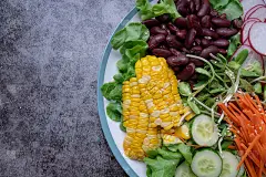 白色大理石桌上摆着一碗蔬菜沙拉，新鲜的绿橡木沙拉，西红柿，玉米，红豆，胡萝卜，红萝卜，橄榄油和黄瓜。