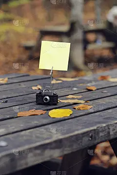 空白纸贴纸与秋天的树叶在老木头的背景。户外书桌古董相机和黄色便条纸