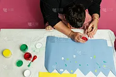 特殊教育的老师和学生穿着长袍，在桌子上用手画着生日花环和涂着丙烯颜料的黄色纸板。塑料工艺疗法。