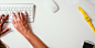 The hands of a designer typing on the keyboard connected to a computer in an office setting.