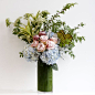 Like a tall drink of water, this refreshing arrangement is undeniably beautiful. Blue hydrangea, pink ice protea, Faith roses, Queen Anne's lace, and burnt palm fans create this vibrant arrangement.