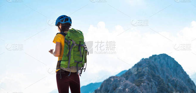 带着背包和头盔的女登山者在夏天爬上山顶之...