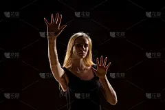 年轻女子挥动着双手。在一个黑色背景的画室里，金发女孩用举起的手表达他们的情感