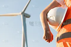 一个工程师手里拿着头盔，橙色的维斯塔站在风车或风力涡轮机的背景上，有复制空间。