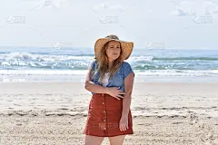 一名30多岁的年轻女子在澳大利亚的currumbin海滩上，戴着一顶大太阳帽，身后是蓝色的海洋