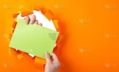 手握绿色sheet与空间设计通过洞在撕裂的橙色纸。