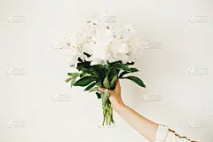 手捧牡丹花束，白墙背景。时髦的白色牡丹在花店的手。你好,春天壁纸。快乐的母亲节。婚礼安排