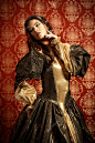 美丽的小姐在郁郁葱葱的昂贵的衣服摆在老式的背景。文艺复兴时期。Barocco。时尚