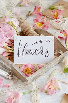 带手写文字的卡片放在粉红色的花之间的木制托盘上