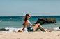 Free photo beach holidays woman back view enjoying summer sun sitting in sand looking happy at copy space. beautiful young model