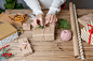 woman-s-hands-wrapping-christmas-gift-close-up-unprepared-presents-wooden-background-with-decor