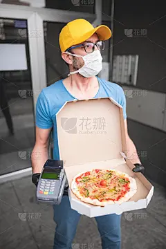 送餐员带着医用防护口罩拿着披萨盒-病毒和大流行的日子，送餐上门。