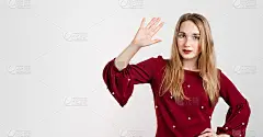 年轻漂亮的金发女郎向我问好，愉快而友好地微笑着，挥舞着她的手。友好的女孩挥手打招呼，面带微笑，见到熟
