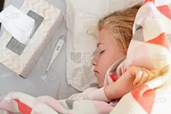 一个生病的十几岁的女孩躺在床上，毯子上盖着温度计