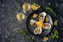 新鲜捕捞的牡蛎，打开的黑色盘子，柠檬片，香草和一杯香槟在黑色的石头背景。放置文本，俯视图。别致的浪漫
