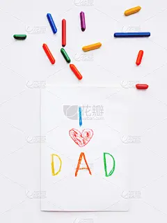 俯视图手绘贺卡为父亲节。孩子用蜡笔写“我爱爸爸”，并画上红色的心形符号。用铅笔平躺在白色的背景上。