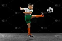 男孩的全身肖像，孩子，足球运动员在统一的训练，踢足球孤立在黑色的背景。