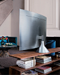 A QLED TV shown with the Gravity Stand is placed on a wooden shelf.