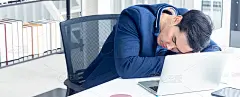 一个年轻的商人坐在一间现代化的办公室里。他感到困倦，因为工作太辛苦了，疲惫不堪。在他的桌子上有一台电