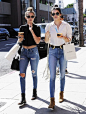 Gigi Hadid wears a fitted black crop top with distressed denim jeans, black boots, sunglasses and a black crossbody bag. Kendall wears a white button-up tucked into high-waisted blue jeans, tan boots and a white fringe bag.: