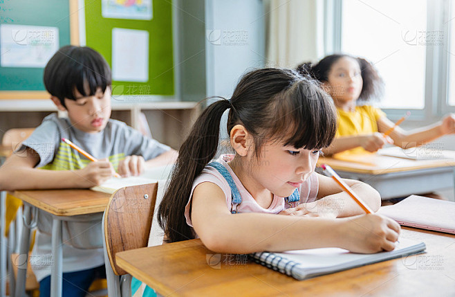 小学生在教室课桌上写字的肖像。在小学做测验的女学生。孩子们在教室里写笔记。教育知识观