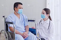 亚洲女医生照顾健康与一名男子病人谁坐在轮椅上的康复室在医院。