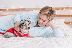 年轻的白人妇女与可爱的小狗狗躺在床上在家里。宠物主人抚摸着毛茸茸的小伙伴。家畜与人的关系。