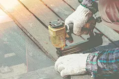 木匠的手或工人的手用空气钉机用木板钻孔。