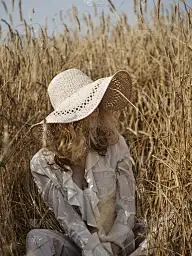 一个穿着白衬衫，戴着草帽的金发女郎坐在麦田里