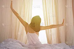 女人在床上伸开双手醒来后，太阳耀斑。深色头发的女人进入一个愉快和放松的一天后，睡了一个好觉和后视图。