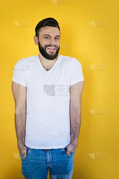 英俊兴奋的现代年轻胡子型男摆姿势与一个宽阔的牙齿微笑在工作室的黄色背景
