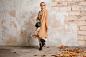 Free photo attractive stylish blonde woman in beige coat walking in street against vintage wall