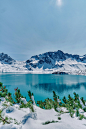A lake surrounded by snow covered mountains under a blue sky