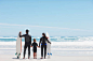 Family in wetsuits with surfboards holding hands on beach