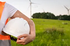 一个工程师手里拿着头盔，橙色的维斯塔站在风车或风力涡轮机的背景上，有复制空间。