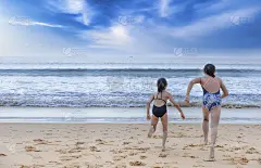 停止运动快乐的两个孩子穿着泳衣从海滩跑向大海。快乐家庭夏日度假理念。两个女孩带着稿子跑去海滩