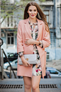 Portrait of attractive stylish smiling woman walking city street in pink coat and floral dress