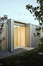 a small building made out of metal and glass with doors open on the outside side