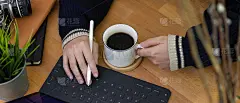 女性自由职业者右手在平板电脑键盘上打字，左手拿着咖啡杯