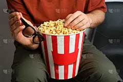 一个男人手里拿着爆米花纸桶和3D眼镜准备看电影。好戏上演。吃美味的不健康的甜食。去电影院看一部新电影