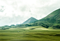 Green pastures stretching to the horizon near a mountain peak