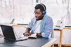 年轻的非洲裔美国人在现代耳机听有声书的教育做家庭作业，黑皮肤的潮人娱乐播放列表上网本写文章的想法