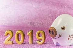 日本新年贺卡的背景是粉色的亮片，上面有可爱的猪或猪动物雕像，以及手工制作的2019年的金色数字。