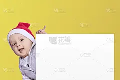 一个戴着圣诞帽的小男孩拿着空白纸。圣诞宝贝带着一张空的白色卡片。复制空间为您的广告和文本