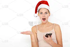 肖像的快乐女性模特戴着红色的新年帽看起来与眼睛，手持现代智能手机，收到意想不到的消息从朋友，读提醒，