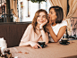 Free photo two young beautiful smiling hipster girls in trendy summer clothes.carefree women chatting in veranda cafe and drinking coffee.positive model shares secret to her friend ear